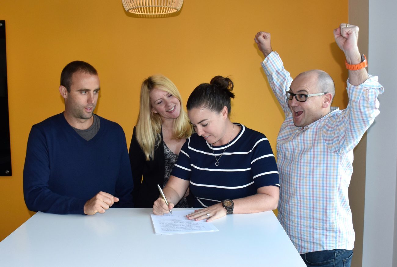 Signing the acquisition agreement, surrounded by a cheering team